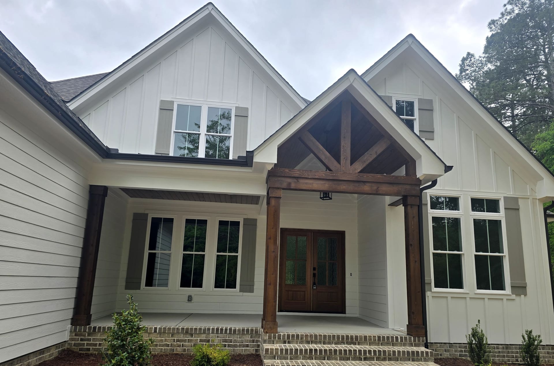 A freshly painted white board-and-batten home with dark trim and a timber-framed entry porch